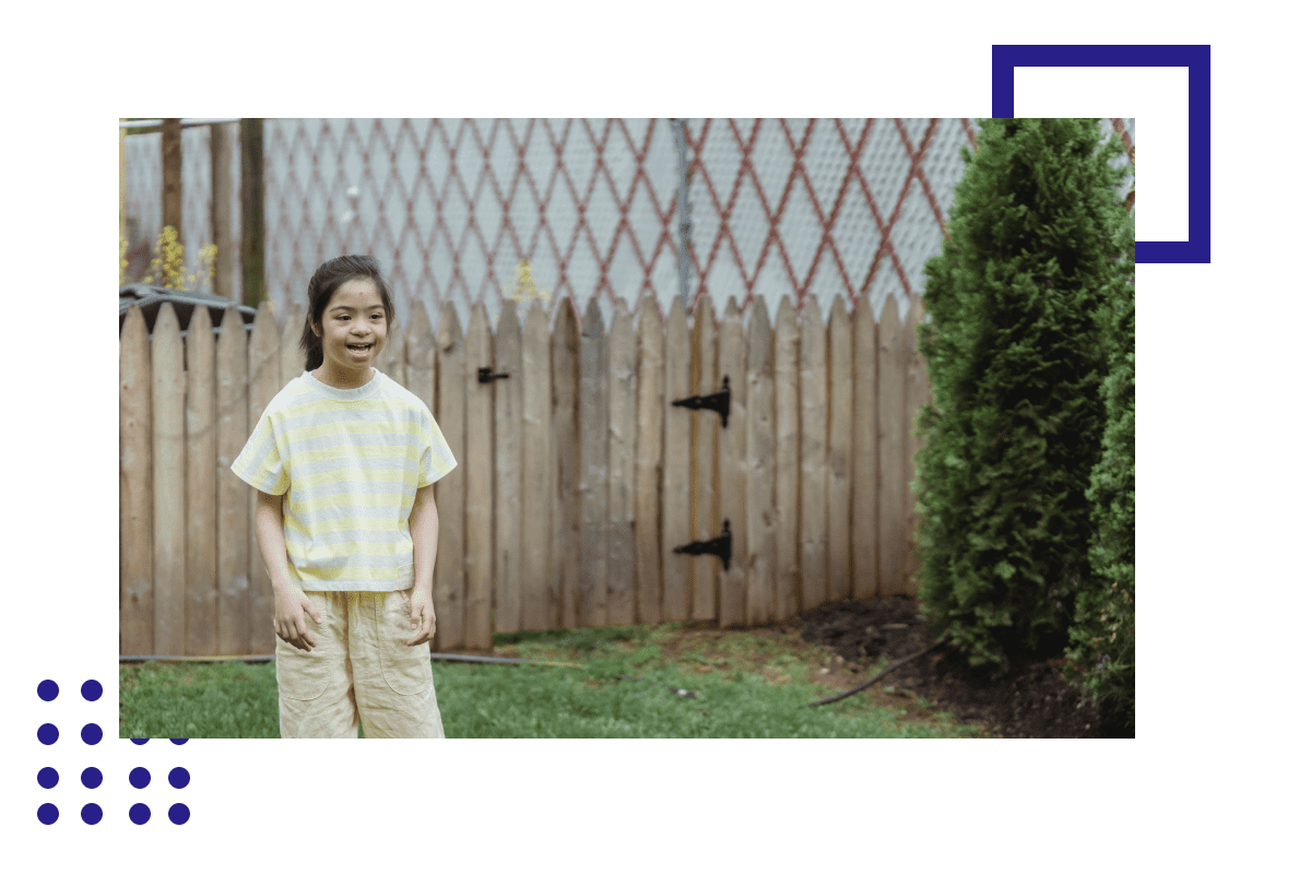 A young girl standing in the grass near a fence.