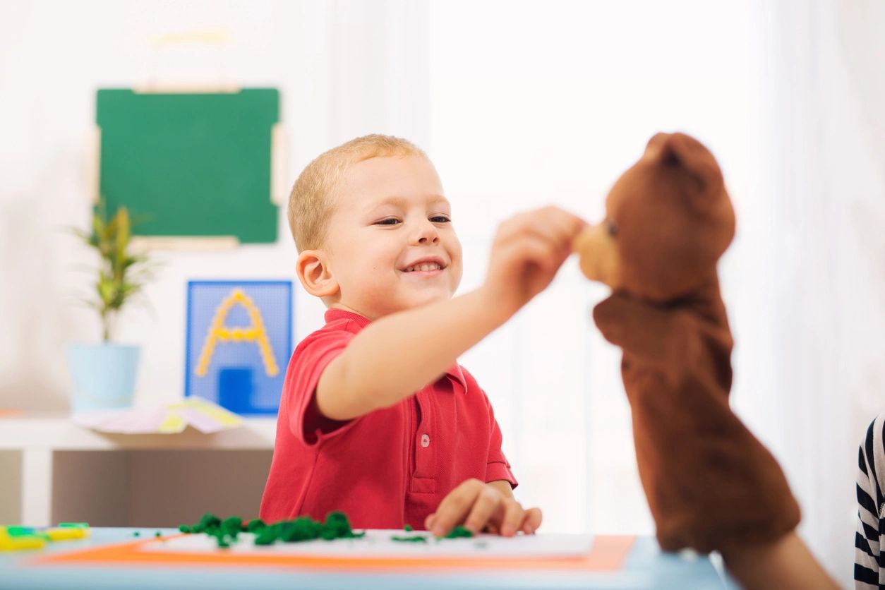 A boy playing with a teddy bear in the classroom.