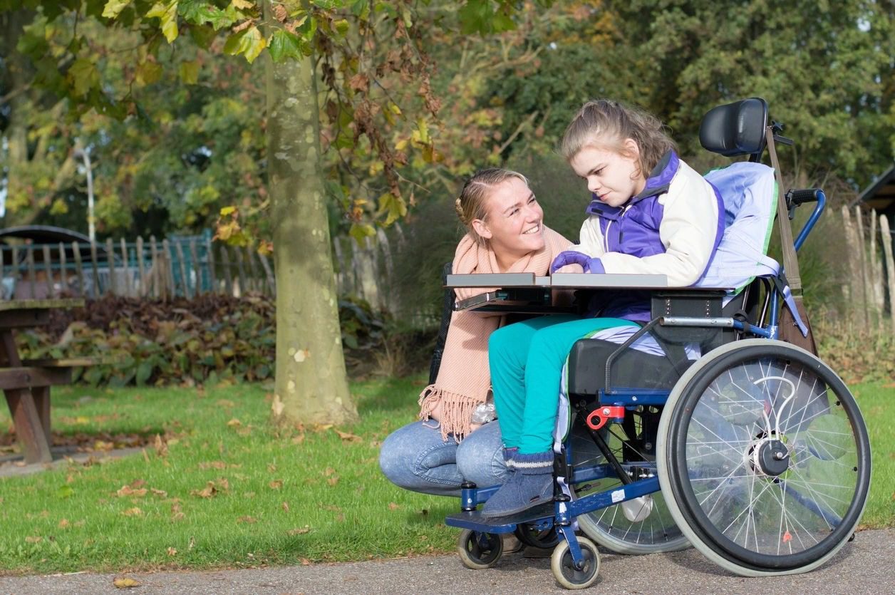 A woman sitting on the ground next to a girl in a wheelchair.