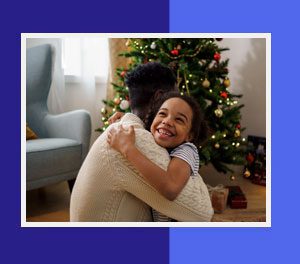 A man and child hug in front of a christmas tree.