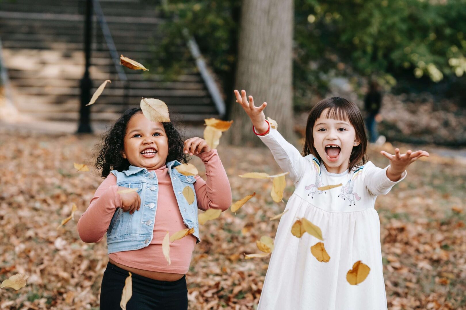 Two young girls playing with leaves in the park.